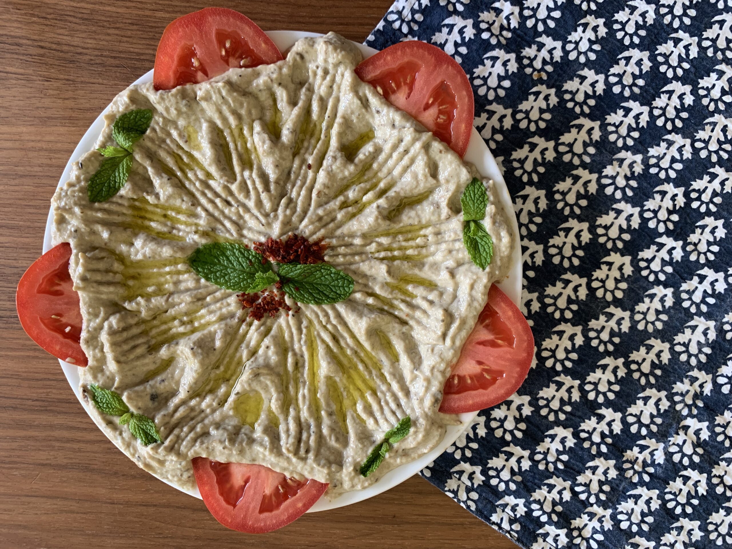 Randa's Mutabal: Syrian Roasted Eggplant and Yogurt Dip A decorative cloth and a plate of soft mutabal with mint, olive oil, parsley, and chili flake garnishes.